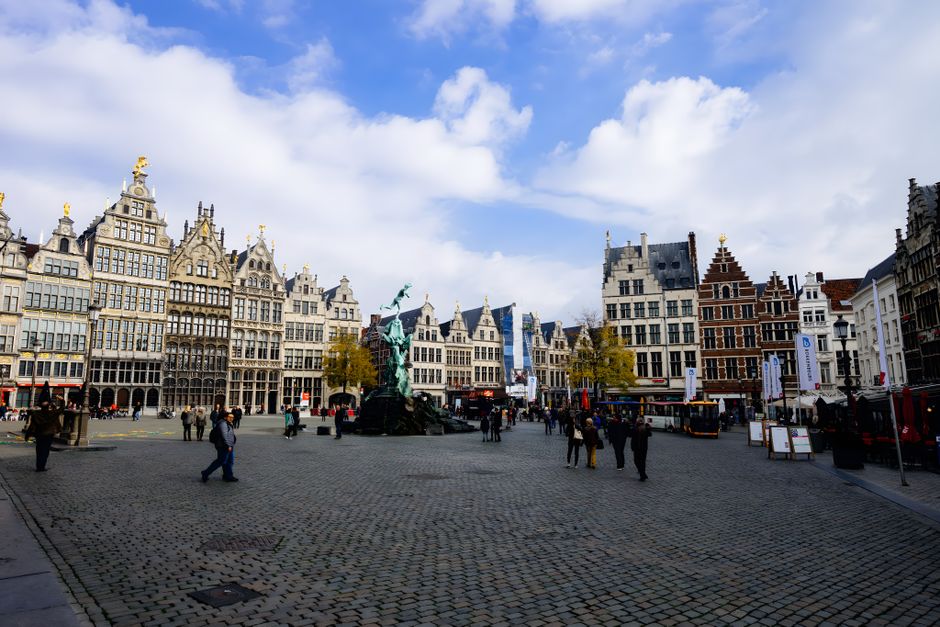 Cobblestone square in Antwerp with historic buildings and Brabo Fountain under a bright blue sky.