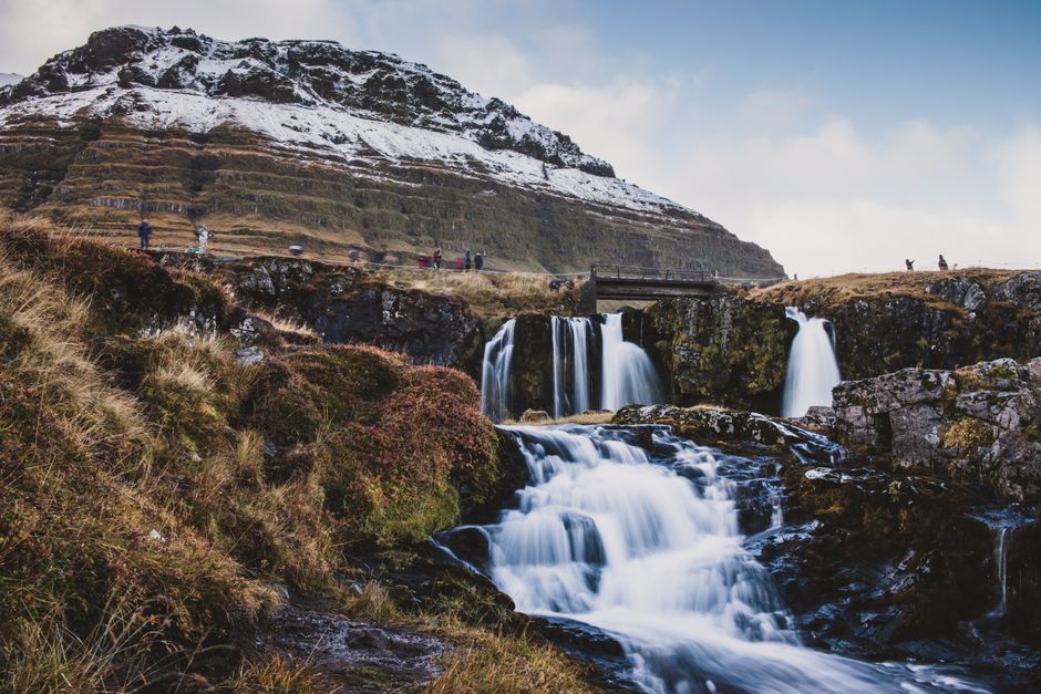 Capture the stunning beauty of Kirkjufell Waterfalls with snowy peaks in Iceland's dramatic landscape.