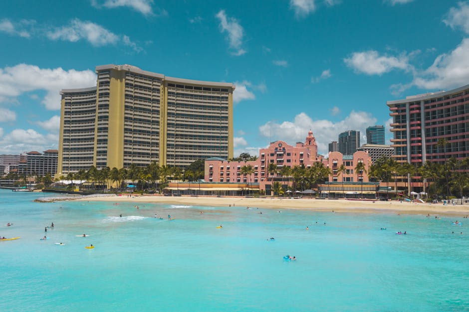Aerial view of surfers and swimmers enjoying Waikiki Beach with iconic hotels in the background.