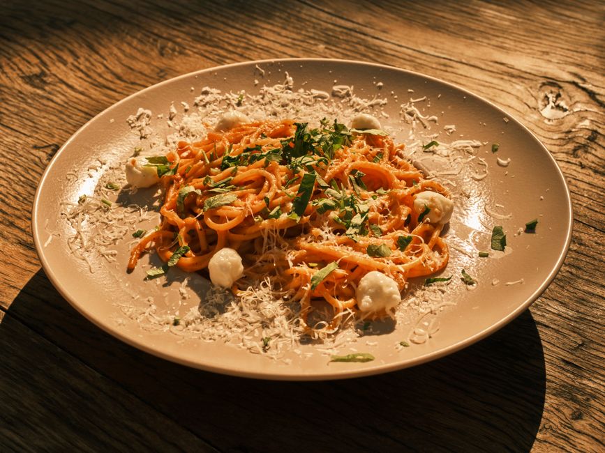 A tantalizing plate of spaghetti in red sauce topped with cheese and herbs on a wooden table.