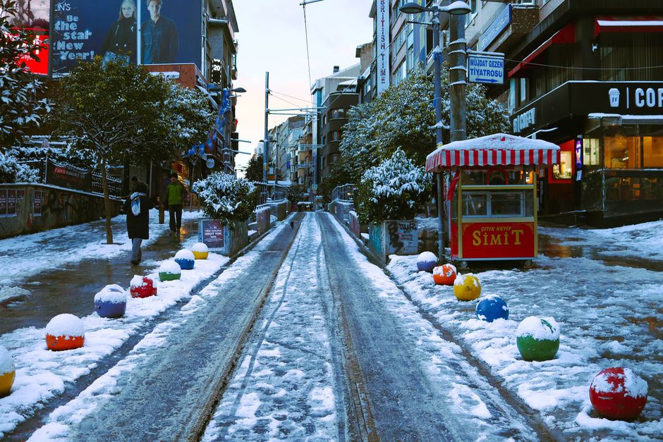 A snowy urban street featuring colorful bollards and a simit stand, creating a vibrant winter scene.