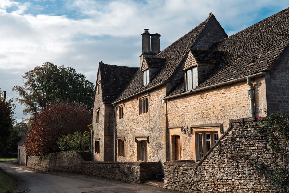 Picturesque Cotswold stone house with autumn trees, classic English countryside architecture.