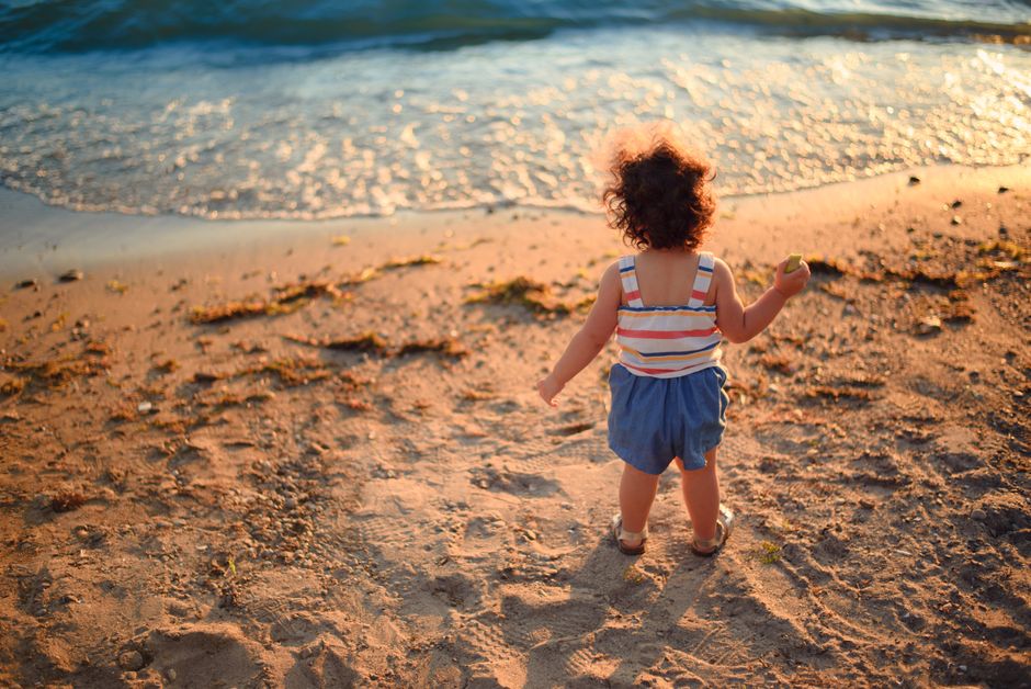 A toddler enjoying a beach outing at sunset with flowing waves and sandy shore.
