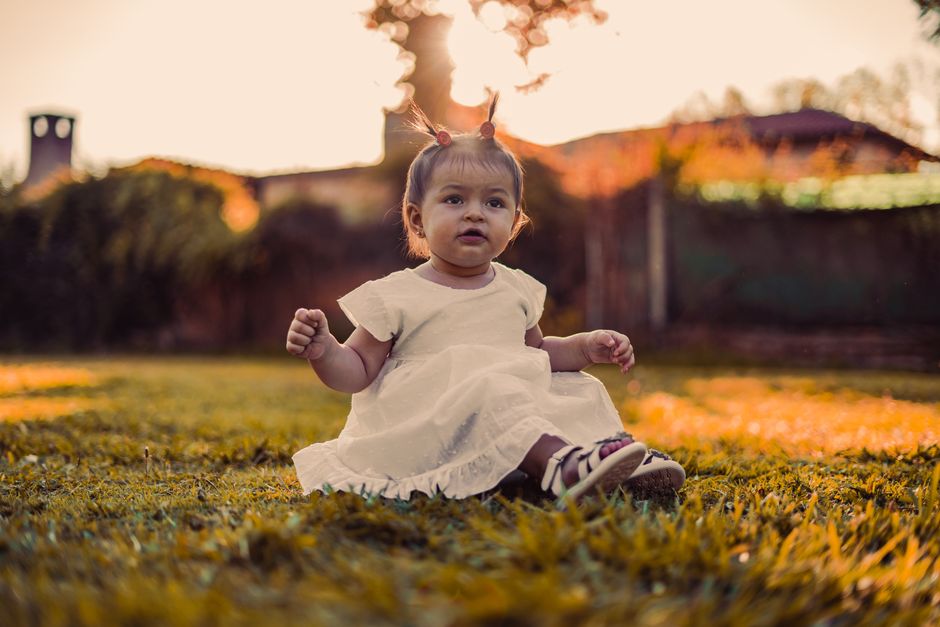 Cute child in white sitting on grass during a beautiful summer sunset outdoors.