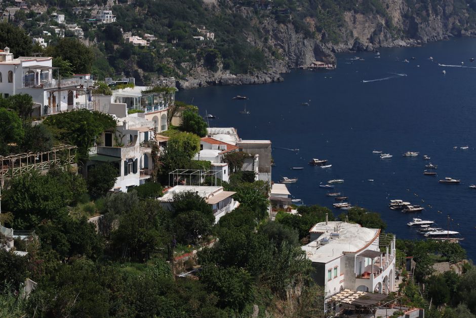 Picturesque view of Italian village on cliffs overlooking the sea, lush greenery and boats.