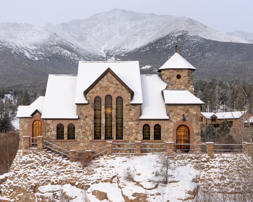 A rustic stone church in Allenspark, Colorado, framed by snowy mountains and winter scenery.