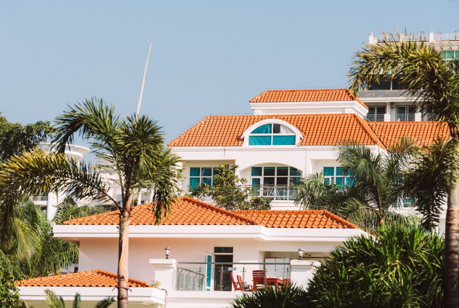 A stunning villa featuring Mediterranean architecture with orange roof tiles and lush palm trees.