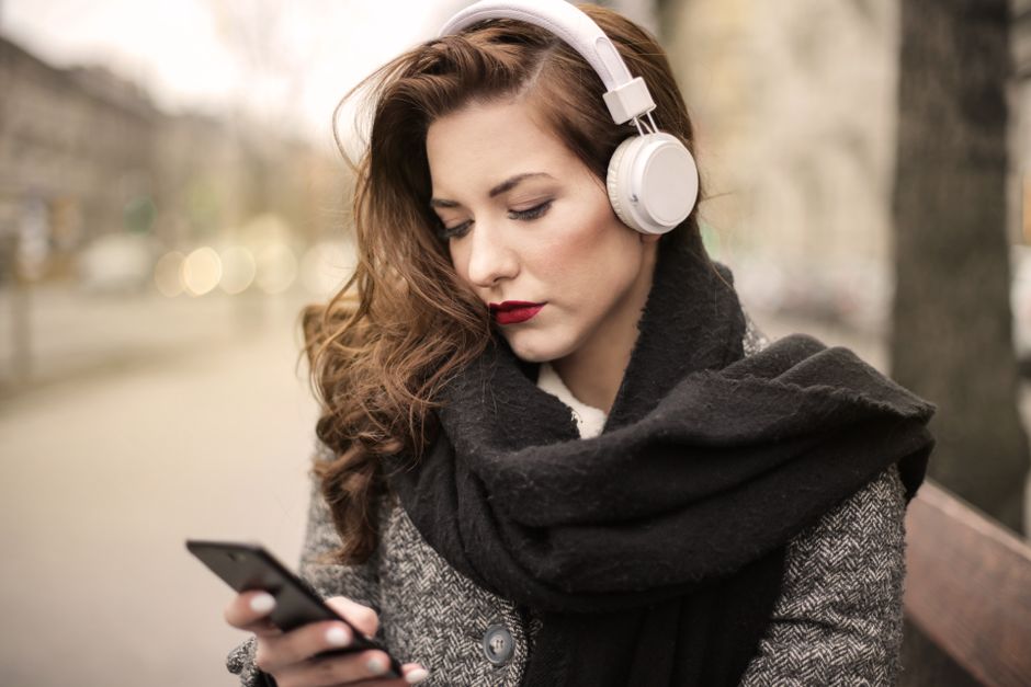 Brunette woman with headphones listening to music outdoors, using a smartphone.