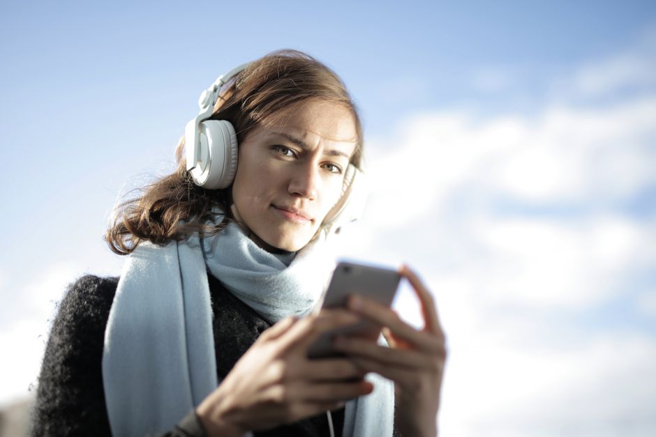 A woman enjoying music on her smartphone with headphones, outdoors in a bright setting.