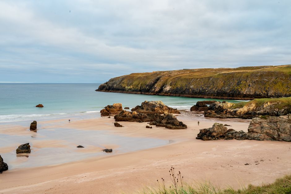 Serene beach scene with rocky formations and calm sea under overcast skies.
