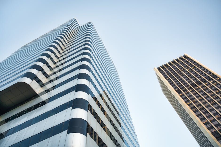 From below of contemporary multistory buildings with modern design located against cloudless sky on street in financial district of city
