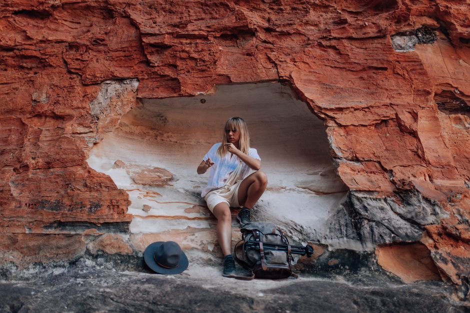 A woman sits on a rocky ledge, surrounded by vibrant red cliffs, exuding a sense of adventure and tranquility.