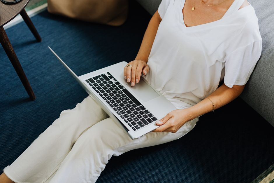 An adult sitting indoors using a laptop on a blue carpet floor, conveying casual work-from-home vibes.