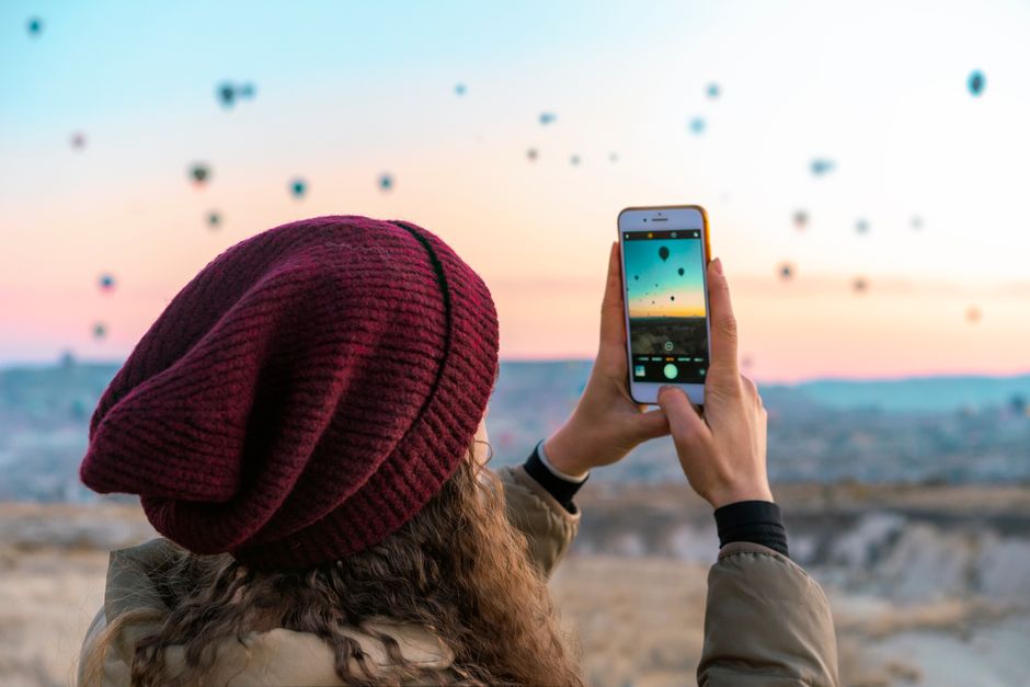 A woman photographs hot air balloons at sunset in Cappadocia, Turkey, showcasing a vibrant and adventurous scene.