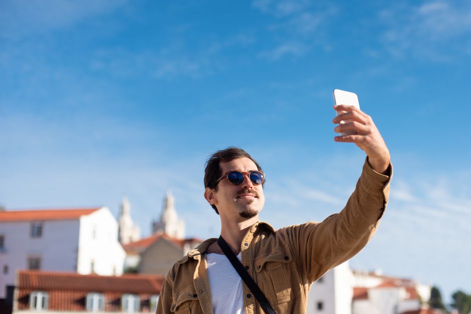 Confident man wearing sunglasses capturing a selfie with clear blue sky background.