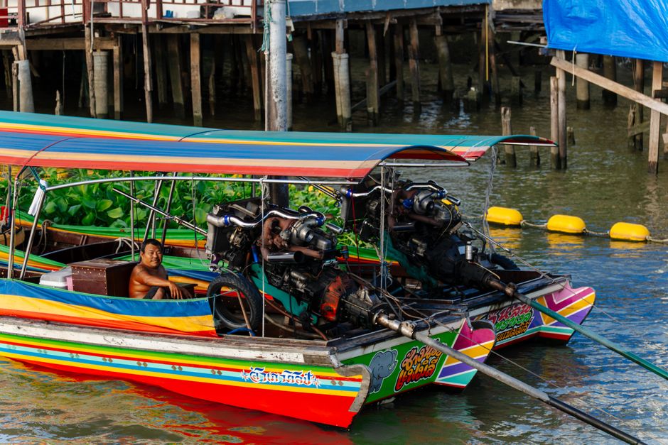 A vibrant long-tail boat with a captain in Bangkok's canals, showcasing local culture.