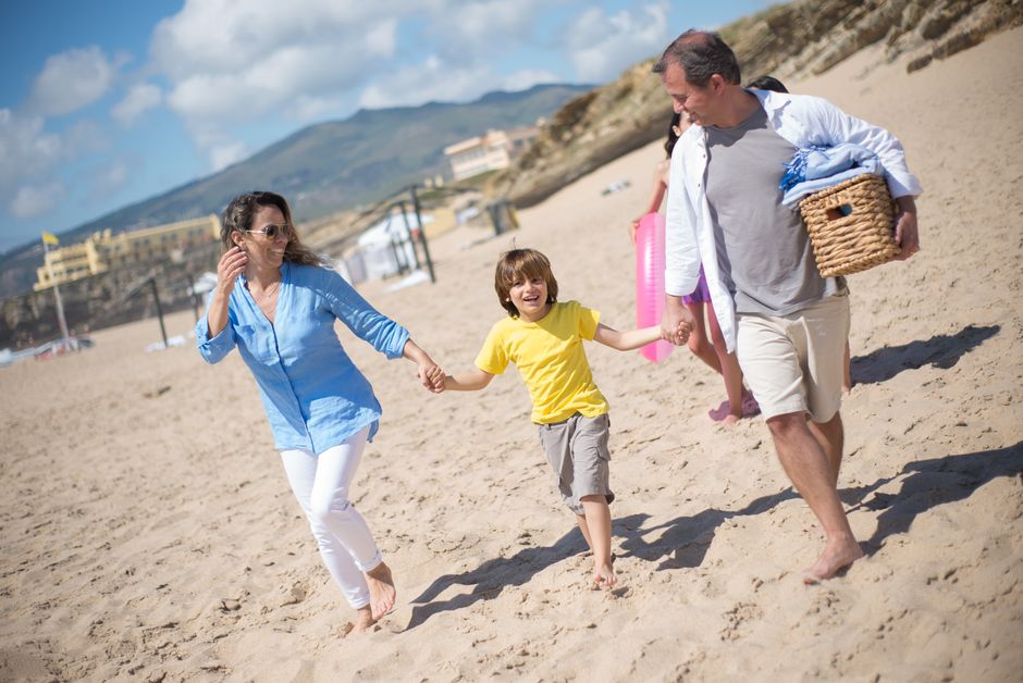 A joyful family strolls along a sunny beach in Portugal, enjoying quality time together.