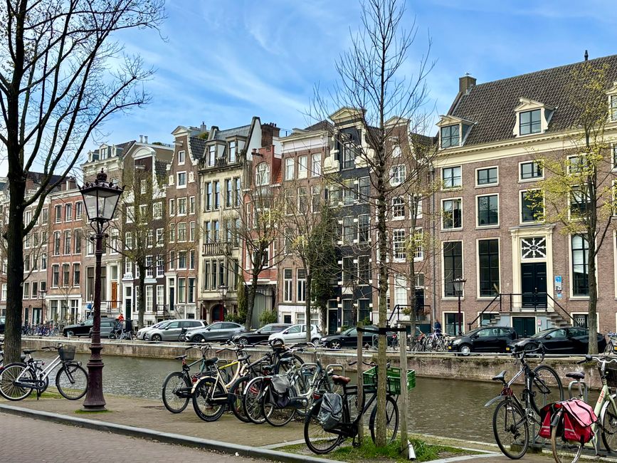 Picturesque view of Amsterdam's canal with traditional houses and bicycles under a clear spring sky.