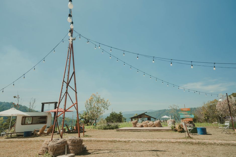 Scenic outdoor area featuring a caravan, string lights, and hay bales under a clear sky.