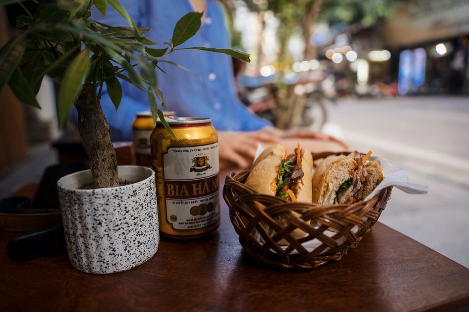 Close-up of Vietnamese banh mi and beer on a Hanoi street-side cafe table, exuding a rustic and authentic vibe.